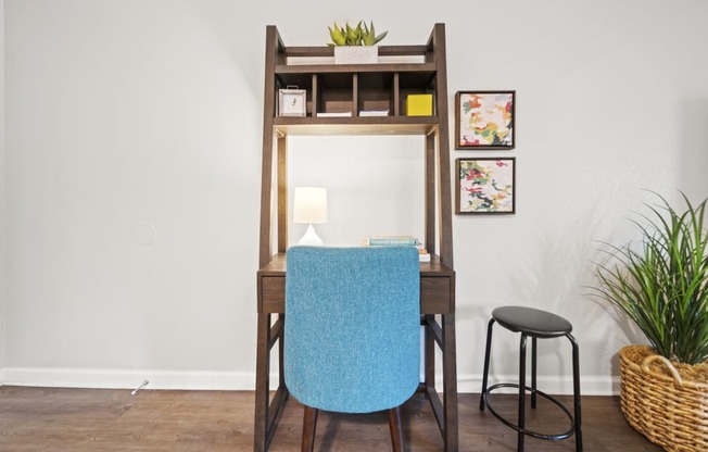 a desk with a blue chair and a black stool in a room with a white wall and