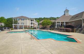 A large swimming pool surrounded by a concrete patio and a building in the background.