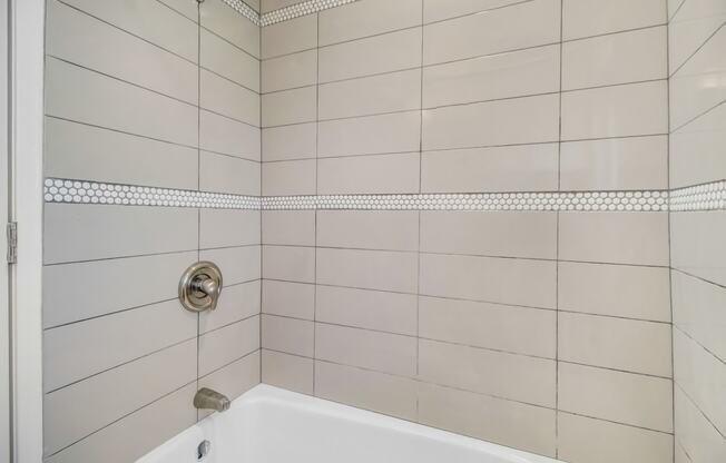 a white tiled bathroom with a tub and shower