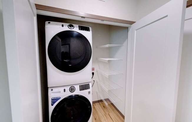 A convenient laundry area here at Van Buren East with a stacked washer and dryer. A built-in shelving system and wood-style flooring create a clean, functional, and organized space.