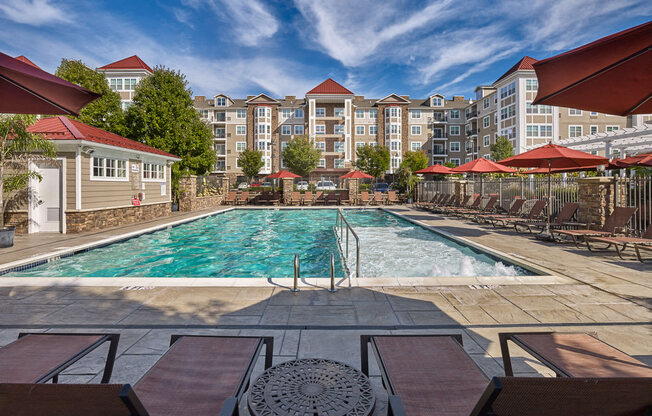 A pool surrounded by chairs and umbrellas with apartment buildings in the background at Vermella Lyndhurst apartments, Lyndhurst, New Jersey