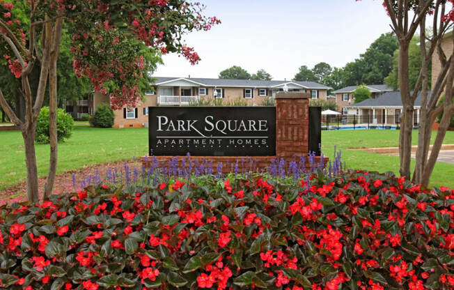 a park square sign with red flowers in front of a building