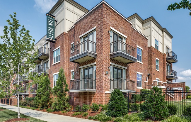 View of Building Exterior, Showing Landscaping, Fenced-In Area, and Balconies at Alpha Mill Apartments