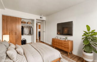 A bedroom with a large bed, a wooden wardrobe, and a TV mounted on the wall.