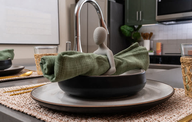 A small green towel wrapped around a grey bowl sits on a plate.