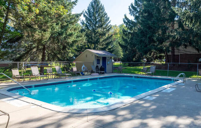 a swimming pool with chairs around it and trees in the background