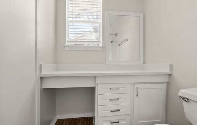 A white bathroom with a window and a mirror.