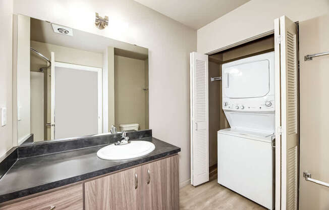 A bathroom with a sink, mirror, and a washer and dryer.