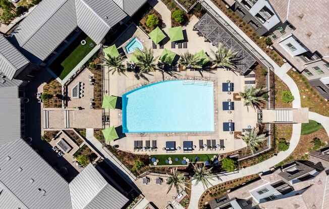 an aerial view of a resort style swimming pool surrounded by palm trees and umbrellas