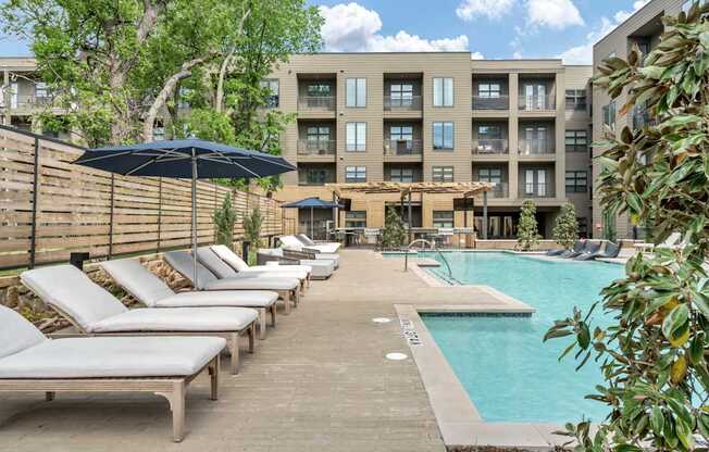 A pool area with sun loungers and a building in the background.