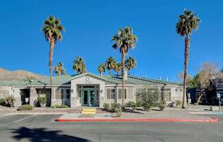 A building with a green door is surrounded by palm trees.
