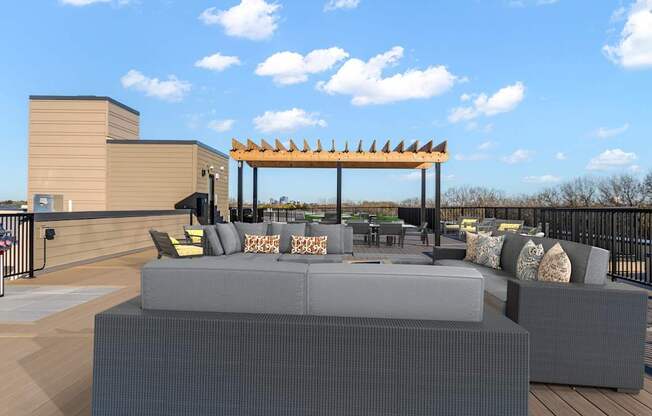 A modern outdoor seating area with grey couches and a wooden pergola.