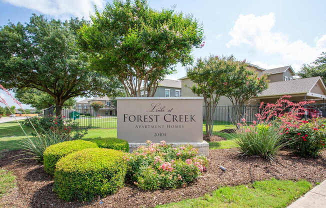 A sign for Forest Creek Apartment Homes is surrounded by greenery and flowers.