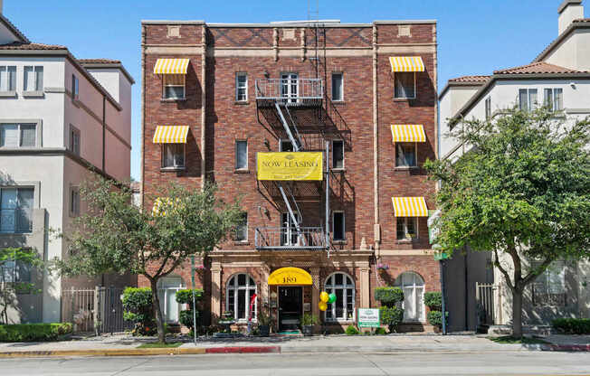 A red brick building with a yellow sign that says Now Leasing at Brookmore apartments in Pasadena, CA.