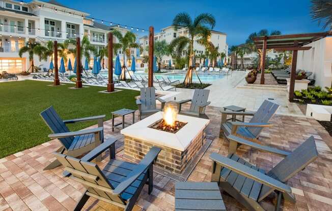 a patio with a firepit and chairs and a pool in the background