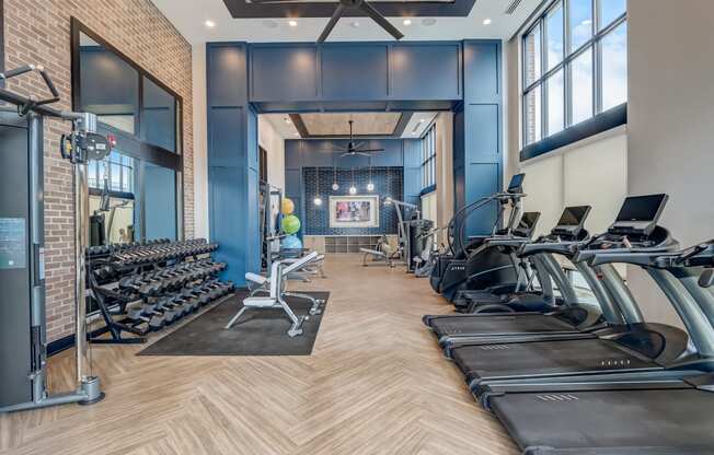 a gym with cardio machines and weights and windows