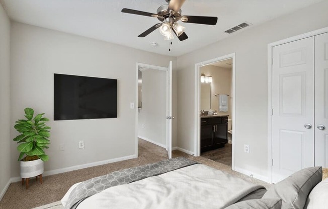 Model bedroom with ceiling fan and attached bath