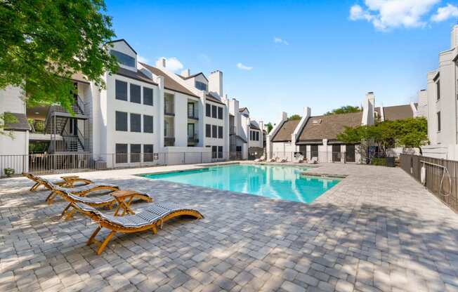 a swimming pool with chaise lounge chairs and buildings in the background