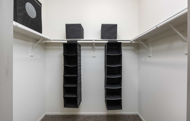 a walk in closet with black shoe racks and a white wall