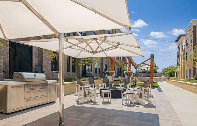 A patio with a grill and chairs under a white umbrella.