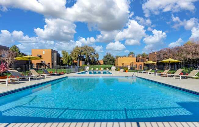 Swimming pool on-site with yellow umbrellas, tables and chairs around to pool deck.  Colorful flowers and landscaping surrounding the pool area.