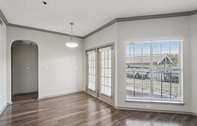 A room with a wooden floor and a large window with blinds.