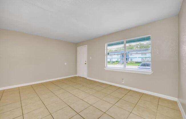 an empty living room with a window and a tiled floor