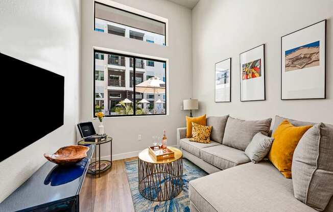 A living room with a grey couch, a coffee table, and a large window.