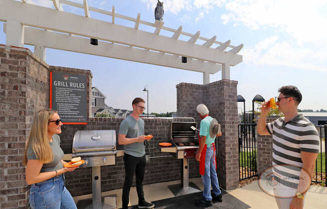 A group of people standing around grills, waiting to get burgers and drinking from orange glasses.
