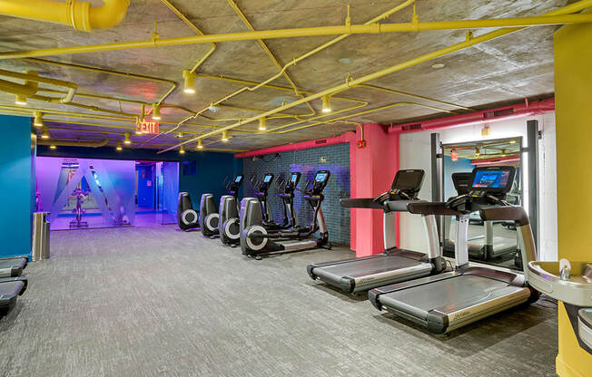 a gym with cardio equipment and a colorful wall in a building