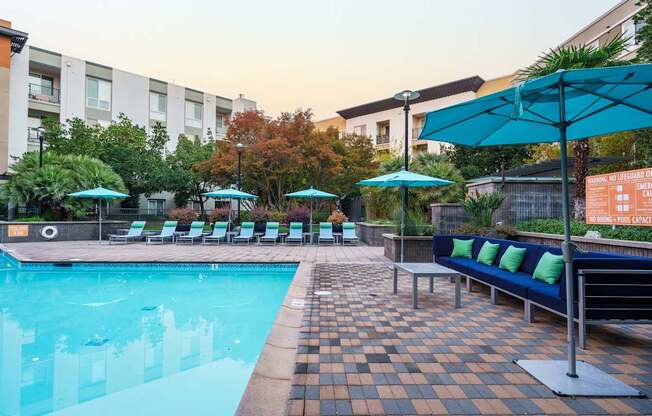 a swimming pool with blue chairs and umbrellas and a building in the background