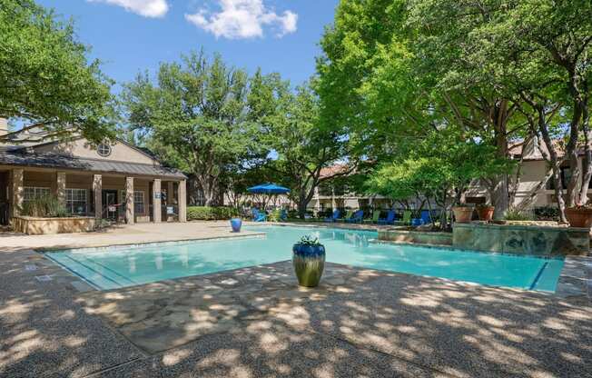 A swimming pool surrounded by trees and the leasing office in the background.