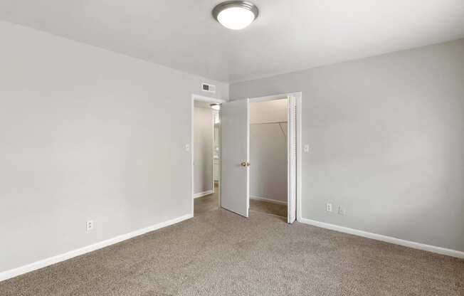 a bedroom with white walls and carpet and a door to a closet