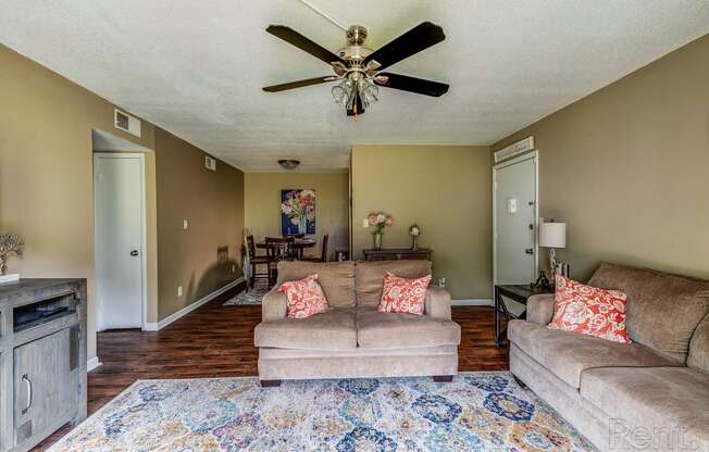 a living room with couches and a rug and a ceiling fan