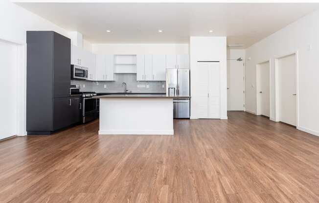 an empty living room with a kitchen and white cabinets