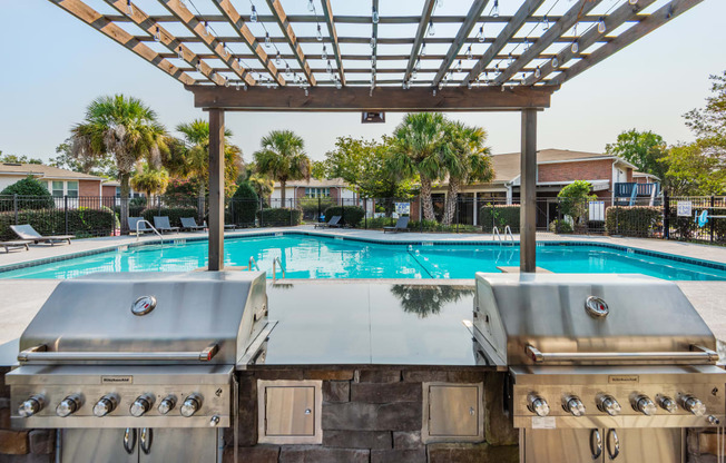 two gas bbq grills with a pool in the background