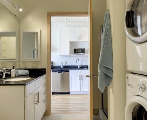 Bathroom with washer dryer stack, stand up shower, toilet in the Flat B studio floor plan at Coze Flats. View of kitchen across the hallway from the open bathroom door.