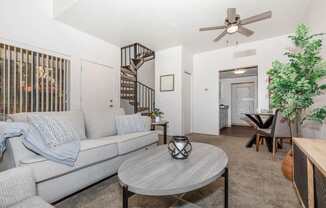 A living room with a grey couch, a round table, and a ceiling fan.