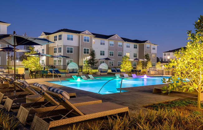 a swimming pool with lounge chairs and umbrellas in front of an apartment building at 55 Fifty at Northwest Crossing, Houston, TX 77092