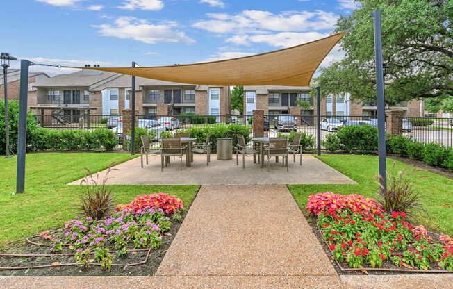 A sunny day at a park with a bench and a table under a shade structure.