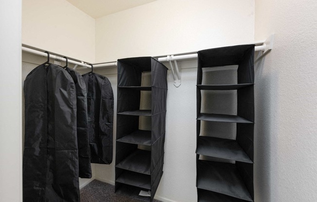 a walk in closet with black jackets and empty shelves