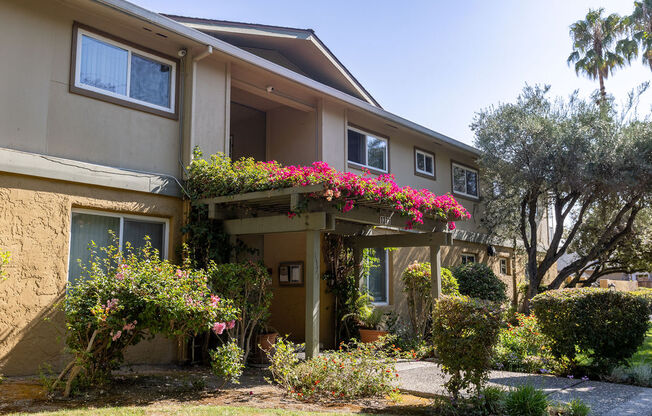 the front of a tan house with pink flowers on it