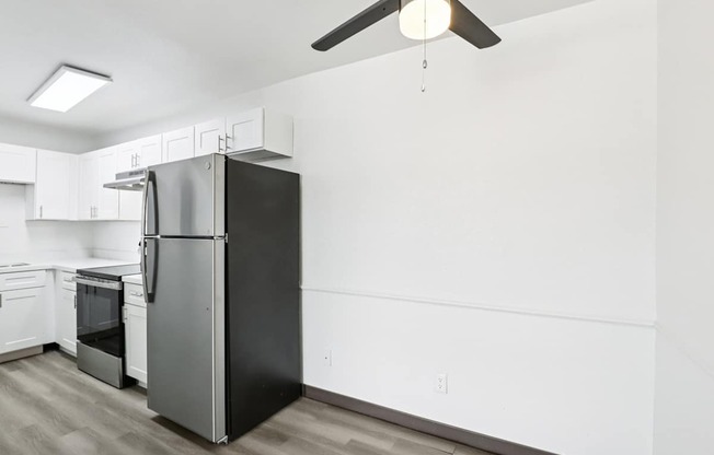 A black refrigerator in a kitchen with white walls and wooden flooring.