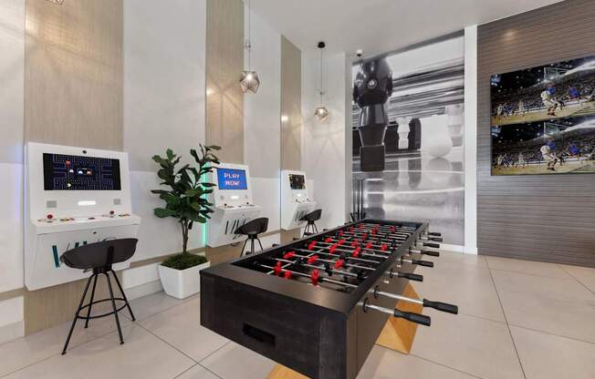 A foosball table is in the middle of a room with a wall of screens behind it.