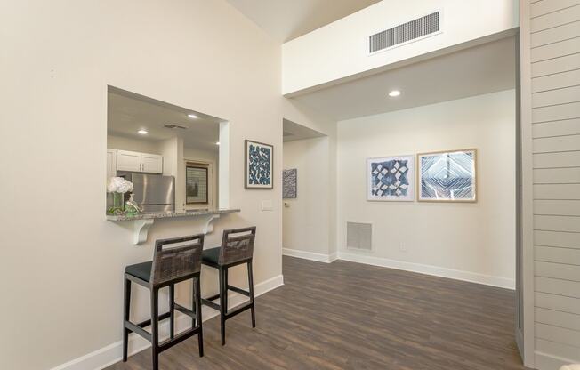 a living room with two stools in front of a kitchen with a bar area