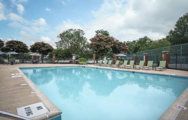 A large swimming pool surrounded by a fence and lounge chairs.