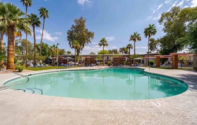 A swimming pool surrounded by palm trees and a building in the background.
