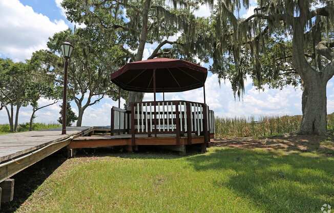 A gazebo with a red roof is surrounded by green grass and trees.