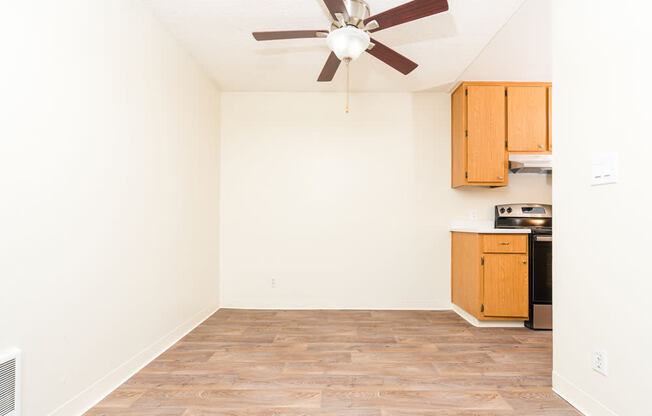 an empty room with a ceiling fan and a kitchen