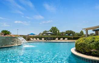 A pool with a waterfall and lounge chairs.